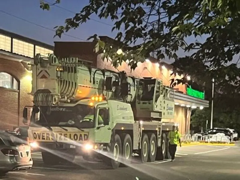 A crane on site for a commercial rooftop HVAC unit installation, at dusk.