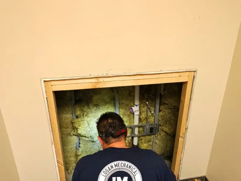 Logan Mechanical technician roughing in mechanical lines inside a wall cavity